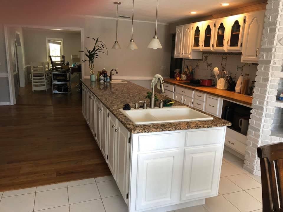 Bright kitchen with white island, granite countertops, pendant lights, and wood floors opening to a dining area