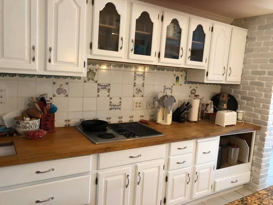 White kitchen with wooden countertops, tiled backsplash, and white cabinets and appliances