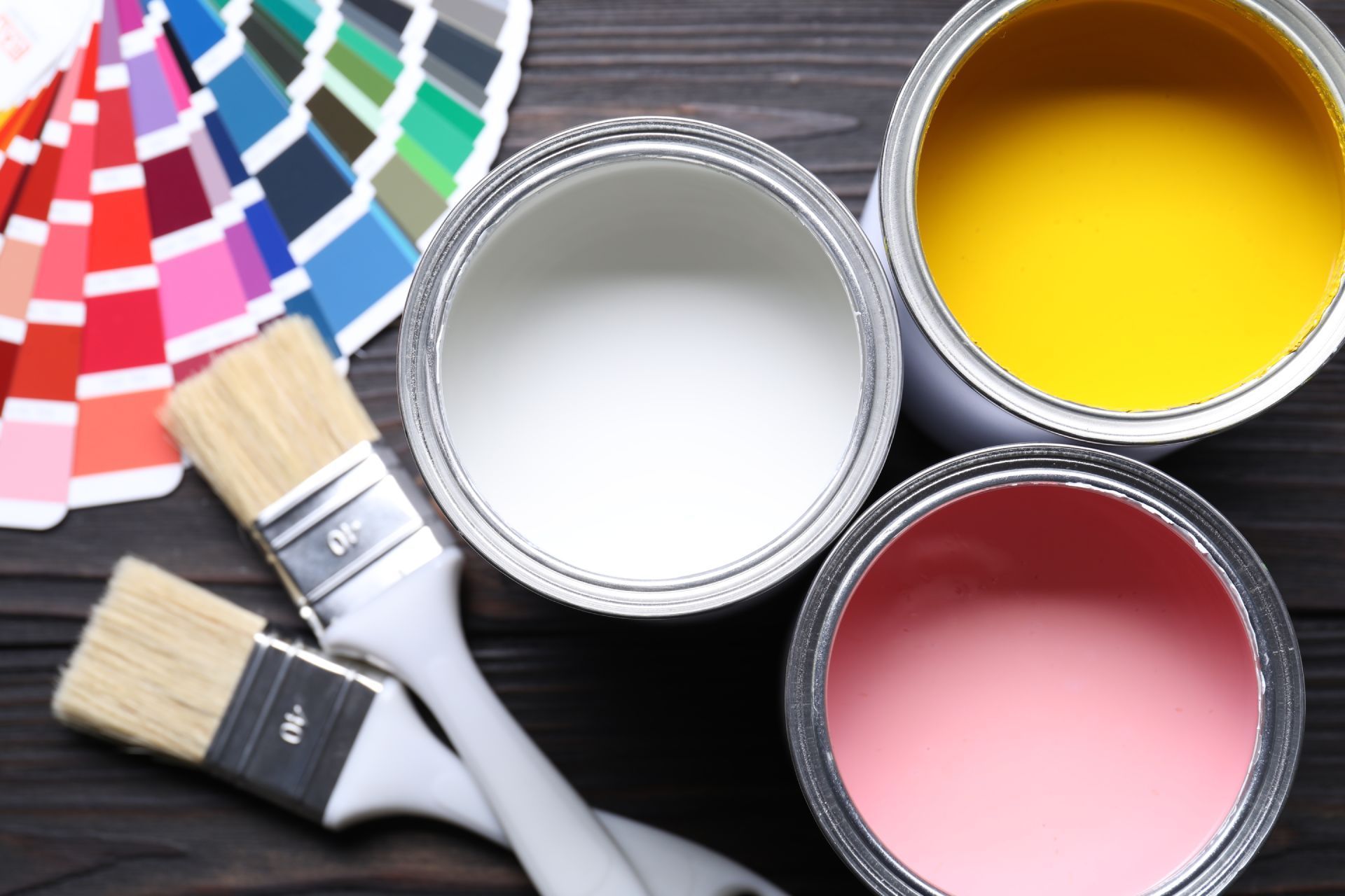 Paint cans and brushes beside color swatches on a dark surface