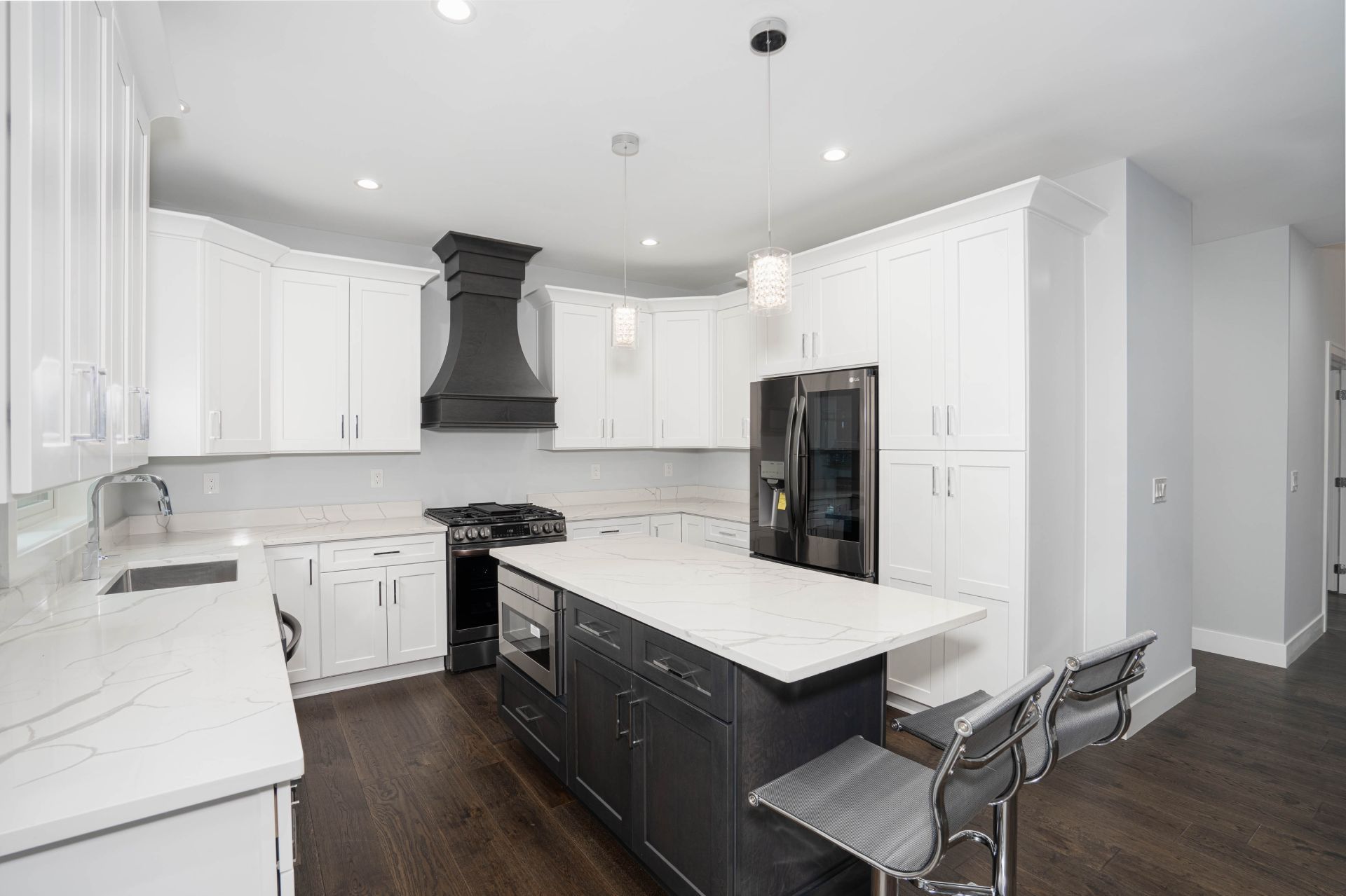 Bright modern kitchen with white cabinets, dark island, stainless appliances, and two bar stools