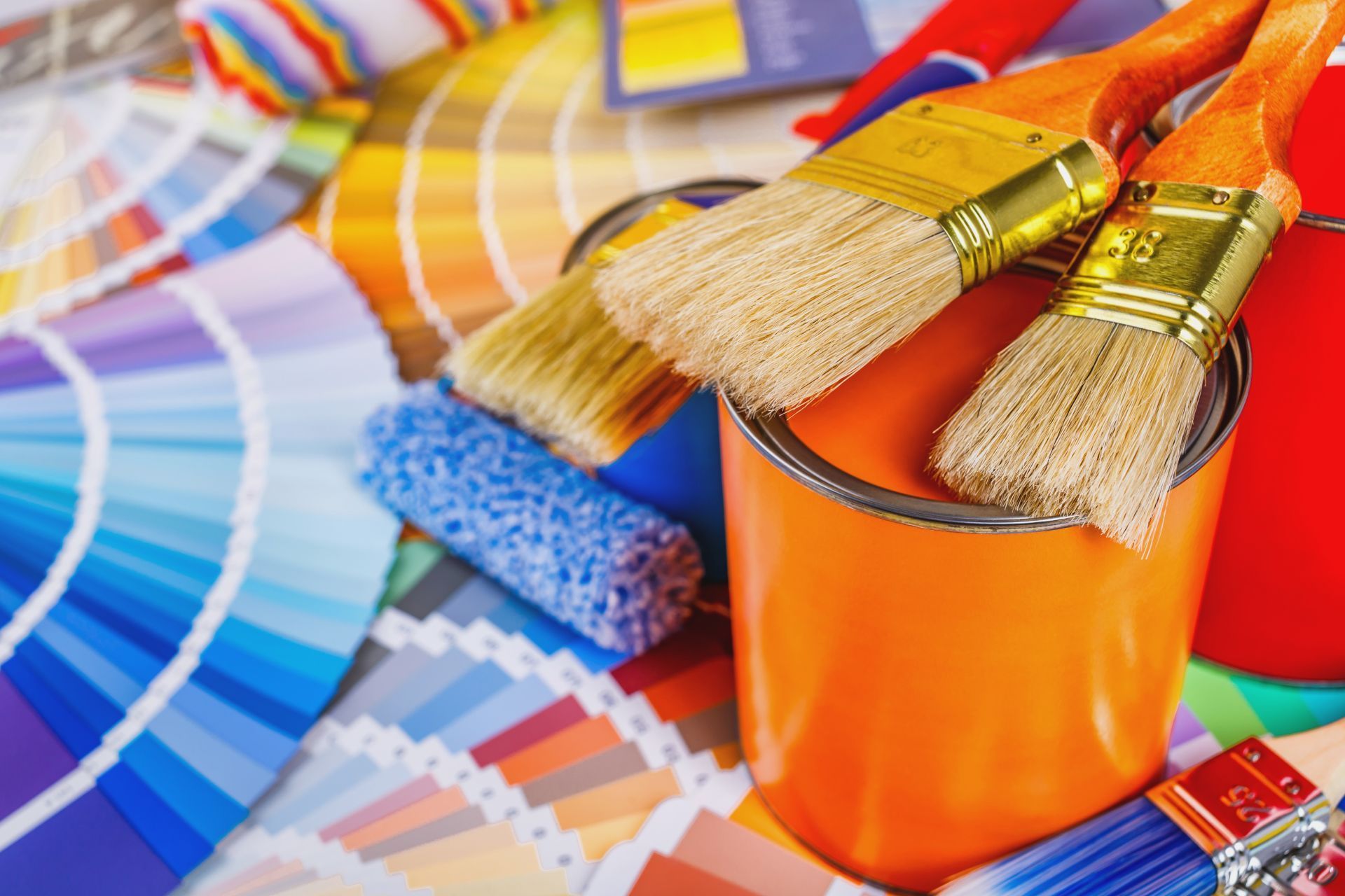 Paintbrushes in orange cup with color swatches and paint samples on a bright art desk