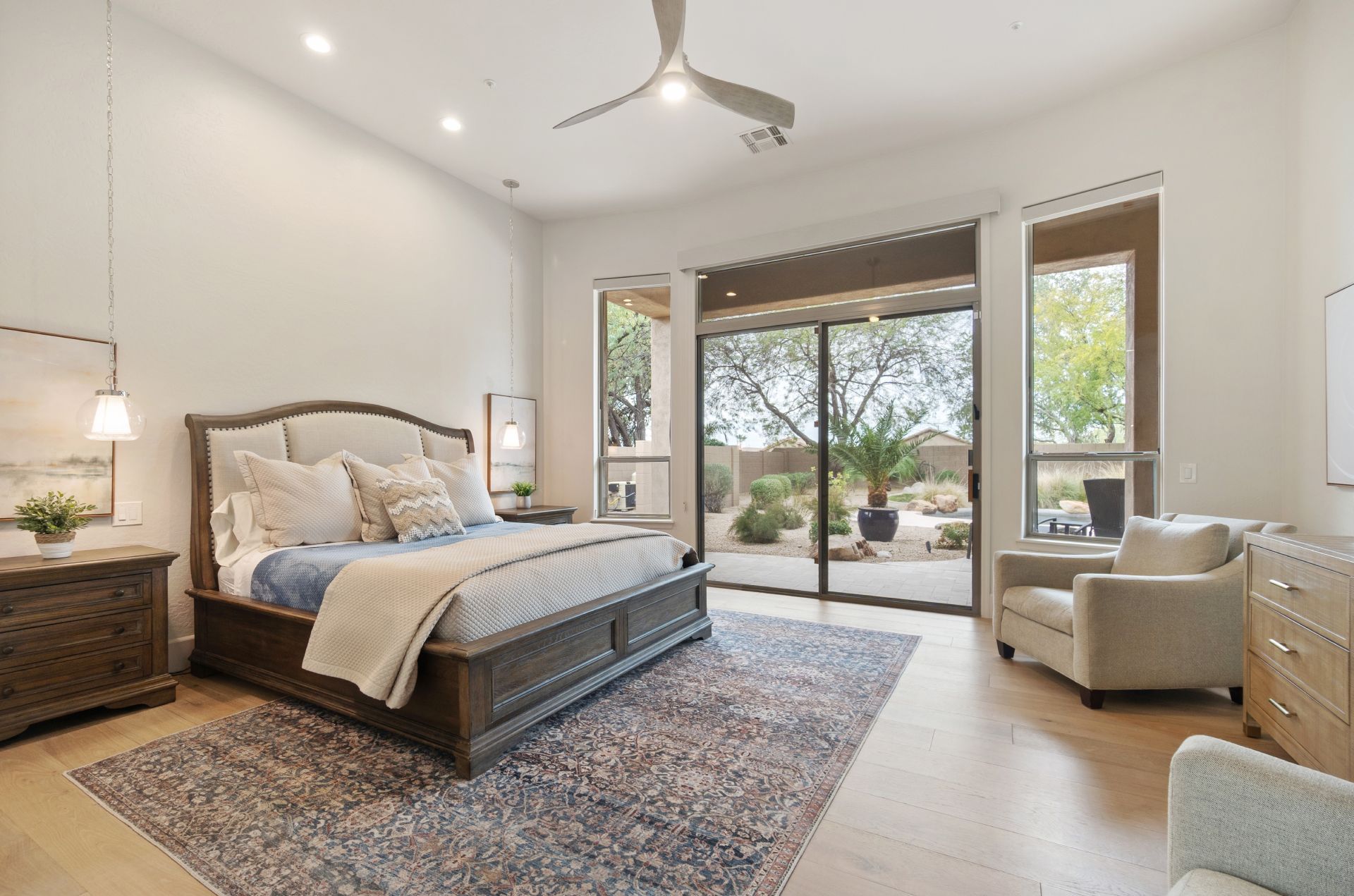Bright bedroom with a large bed, patterned rug, and patio doors opening to a sunny backyard.