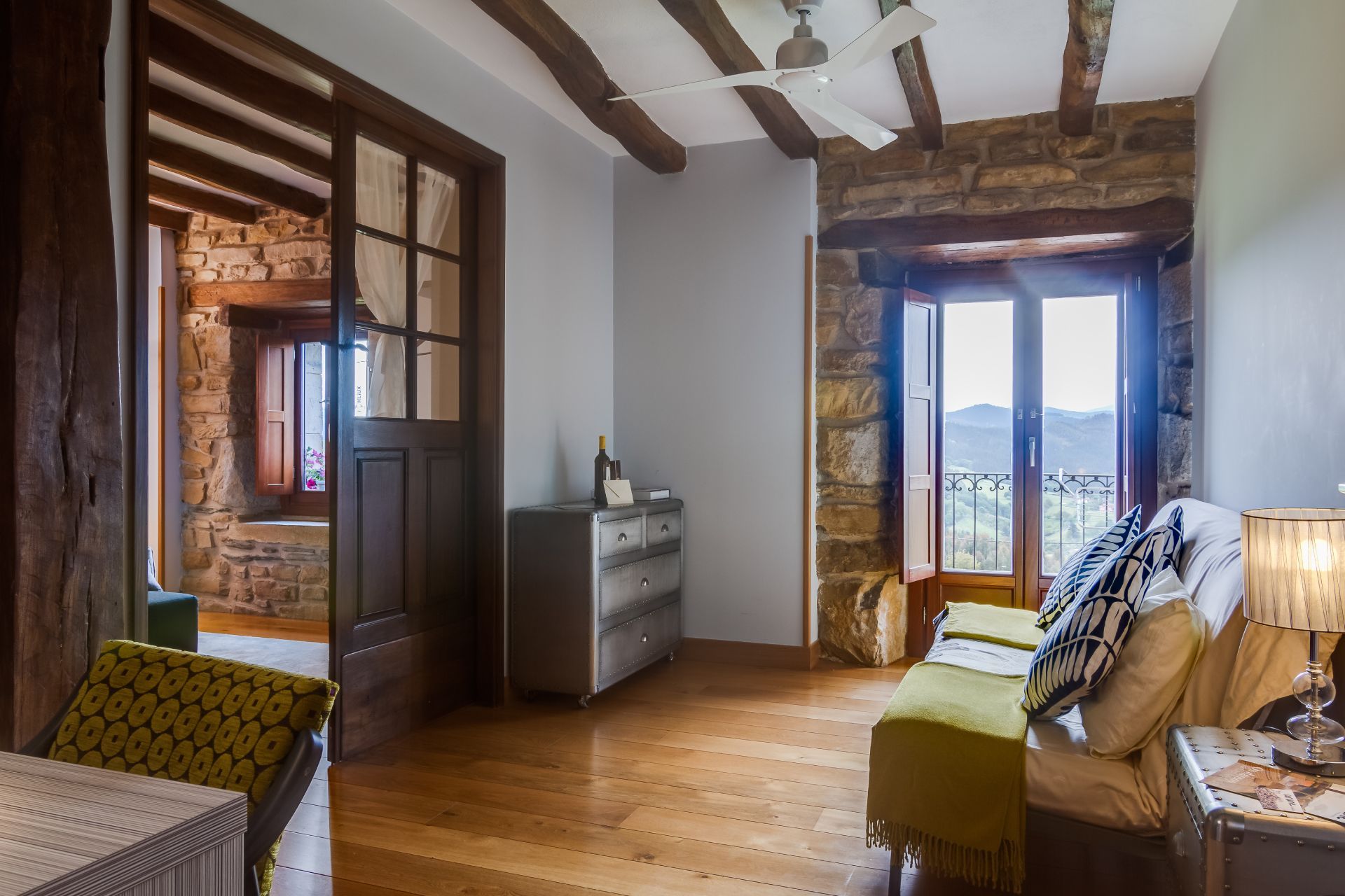 Cozy rustic living room with wooden beams, hardwood floors, dresser, sofa, and balcony doors overlooking mountains