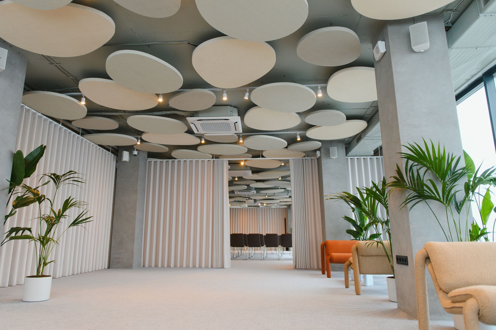 Modern lounge interior with circular ceiling panels, plants, and beige seating area