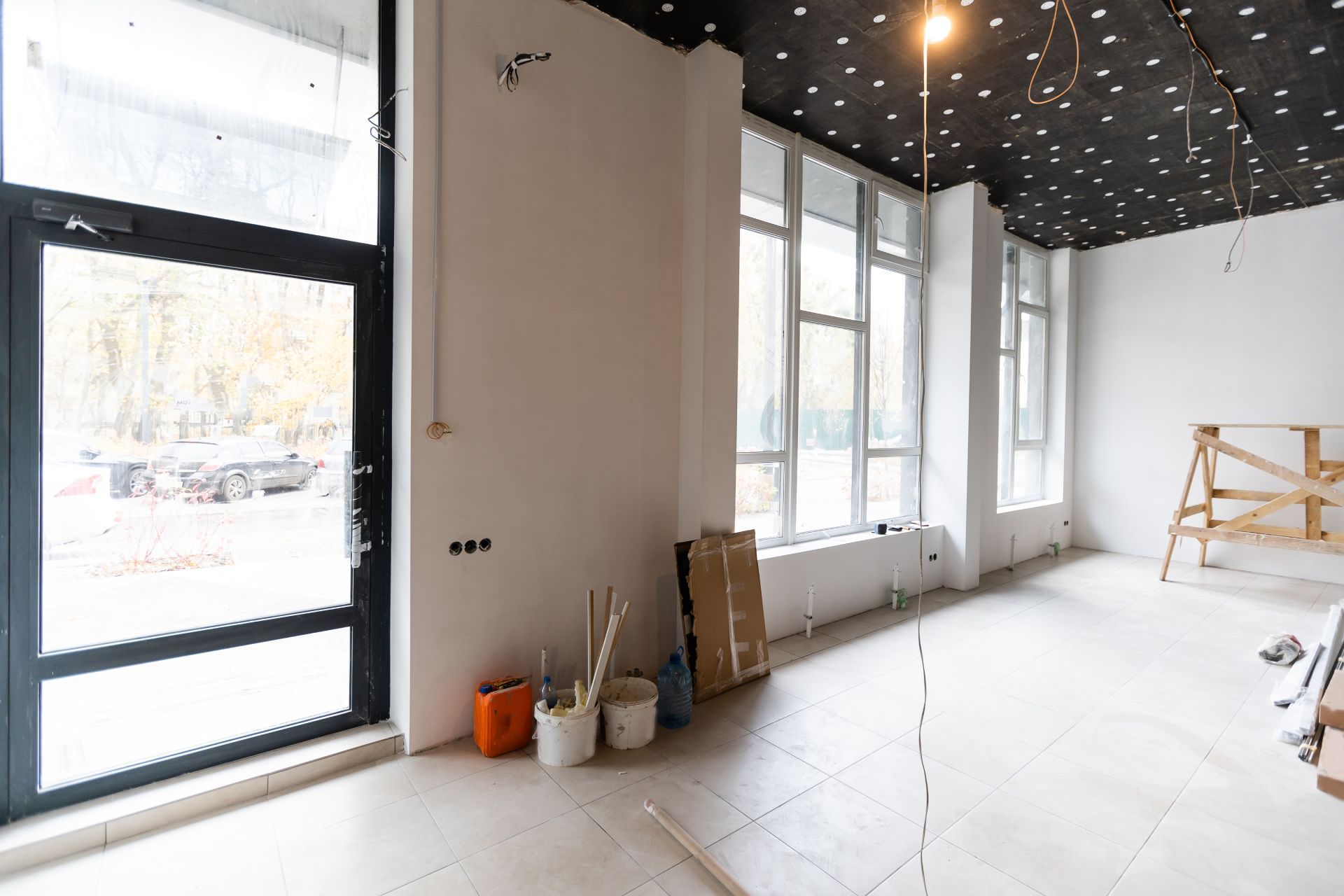 Empty white storefront interior under renovation with large windows, buckets, and construction materials