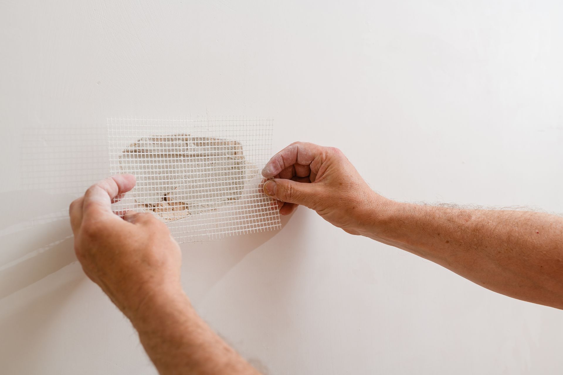 Hands peeling off a transparent adhesive patch from a white wall