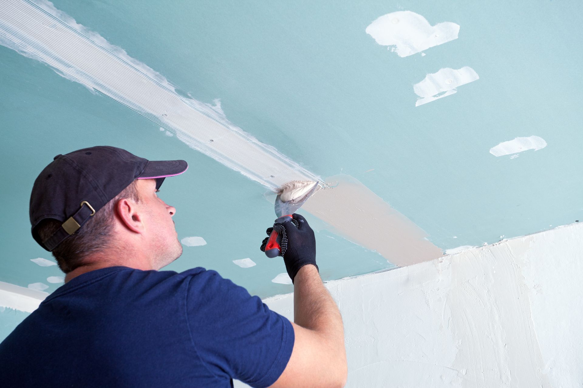 Person painting a light blue ceiling with a roller while standing on a ladder