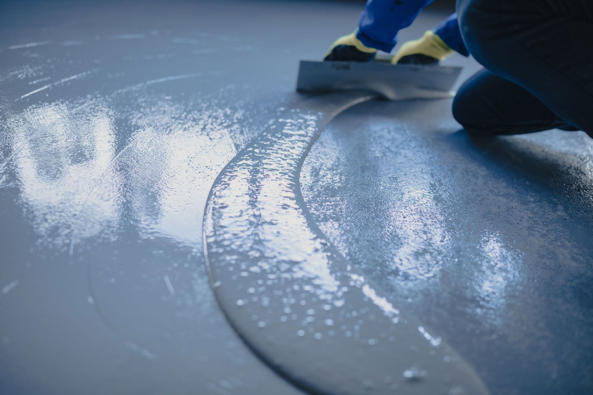 Person smoothing wet gray flooring with a squeegee, leaving a glossy clean surface