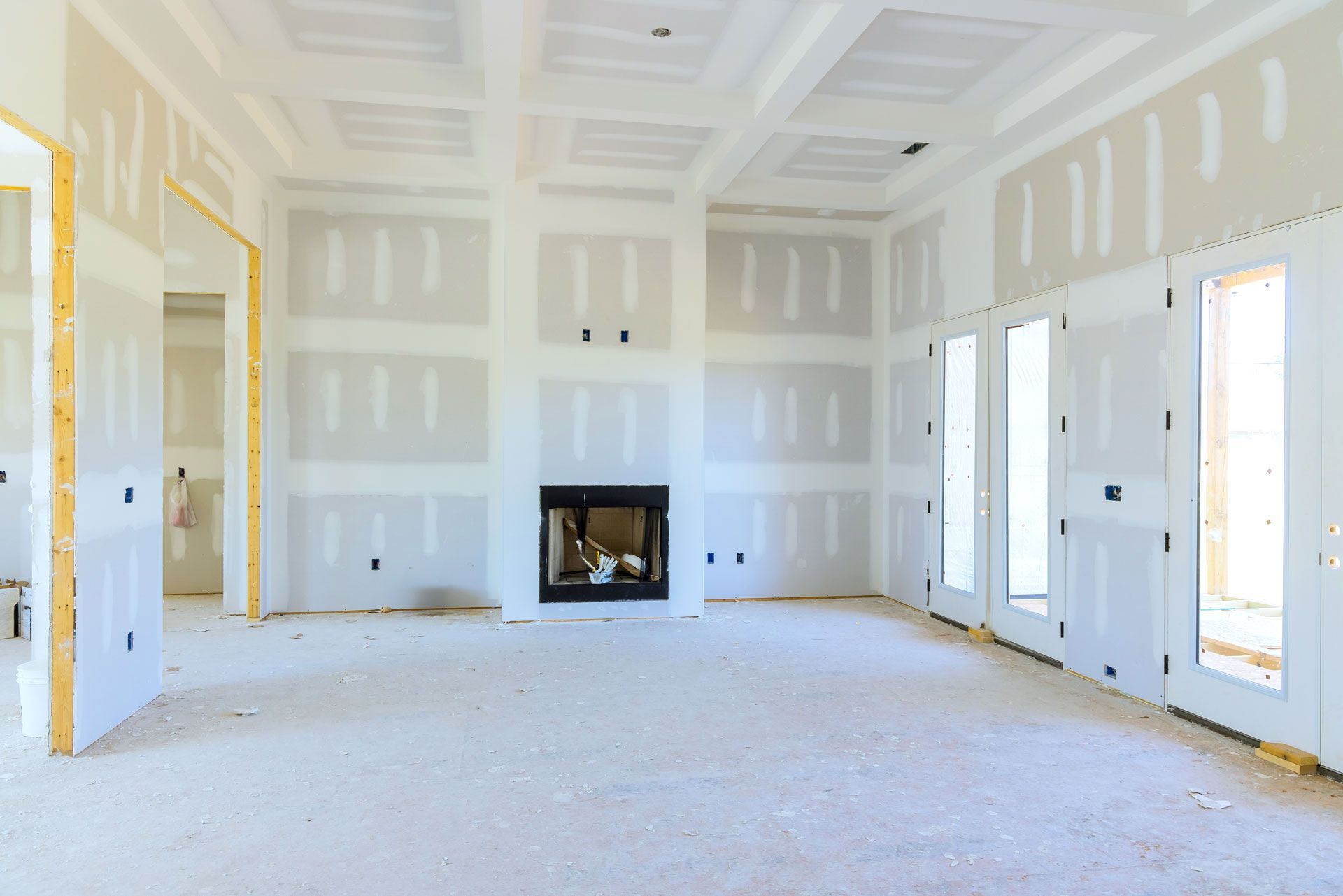 Empty unfinished room with drywall, large windows, and a small fireplace centered on the far wall