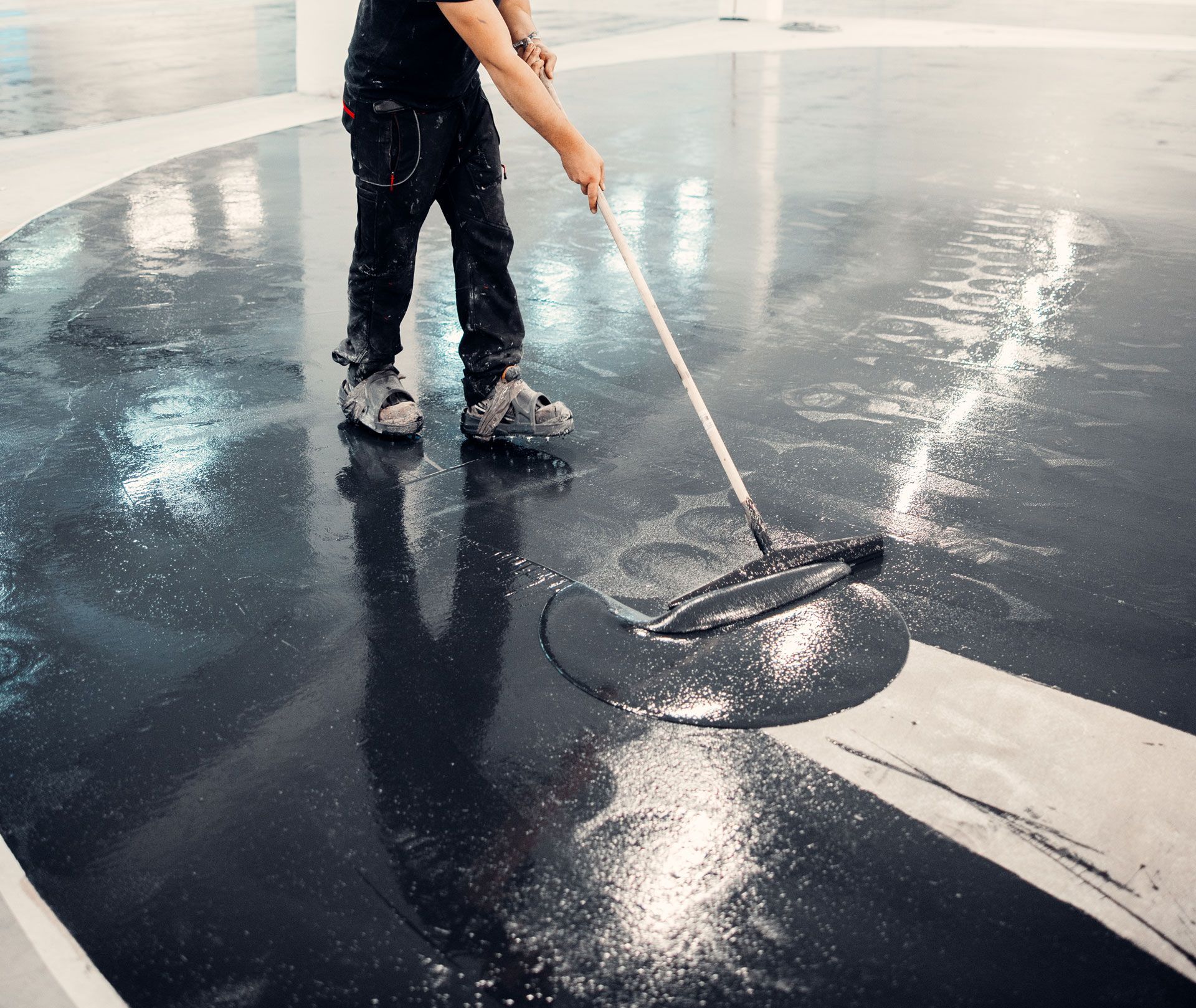 Person smoothing glossy black floor coating with a long-handled applicator indoors