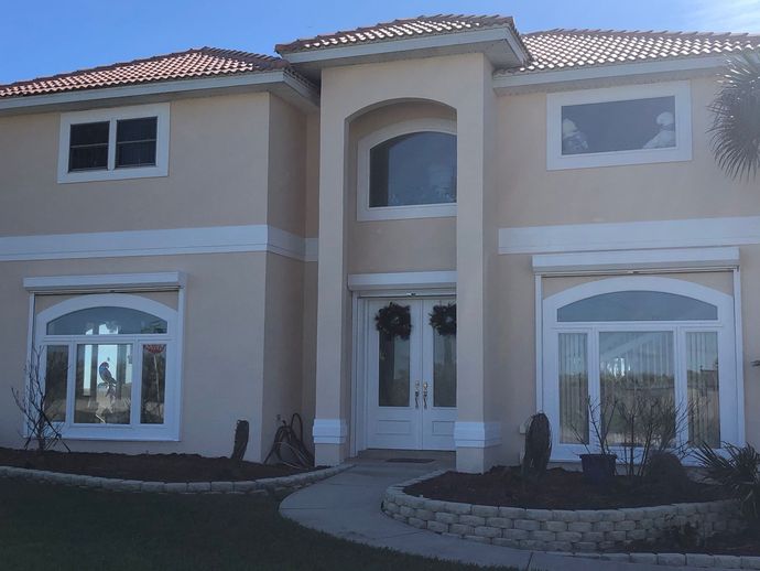 Modern white house with red accents, patio furniture, and a large shaded terrace under a blue sky