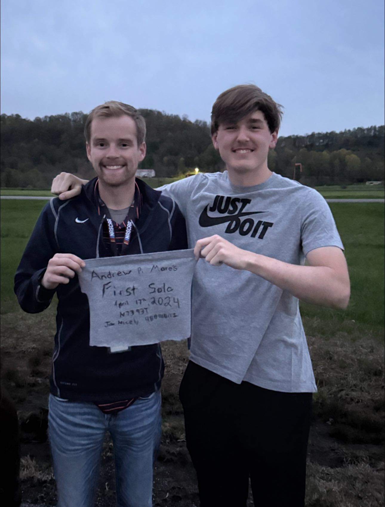 Two men standing outside, one holding a sign that says 