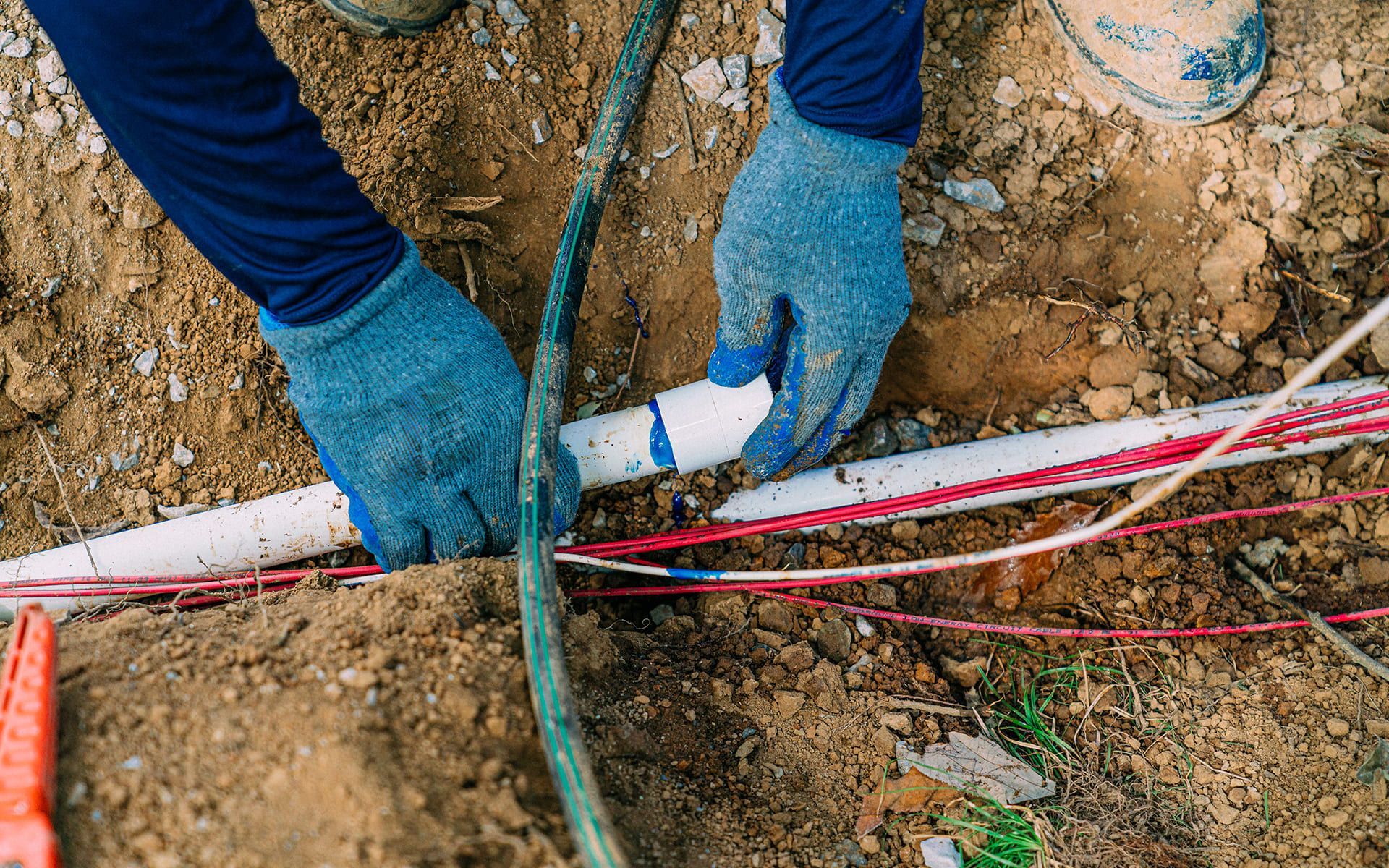 A person is working on a pipe in the dirt.