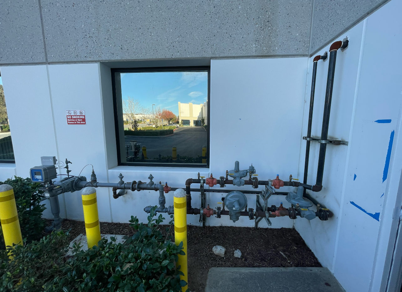 A white wall with a window and a bunch of pipes on it