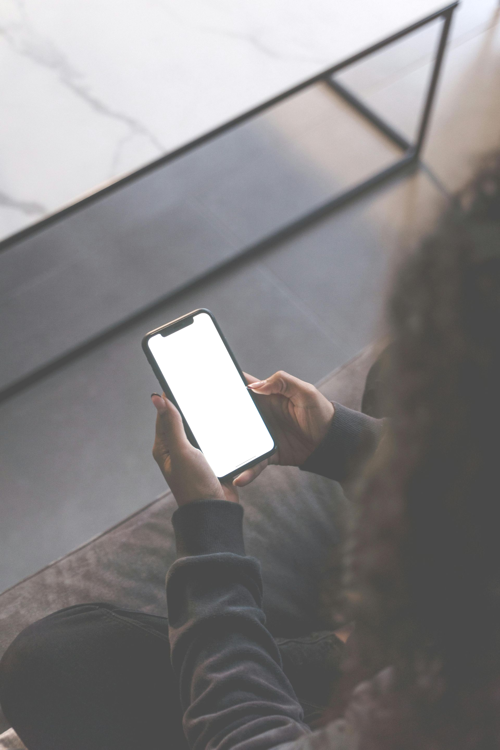Person holding a smartphone with a blank white screen, sitting near a table.