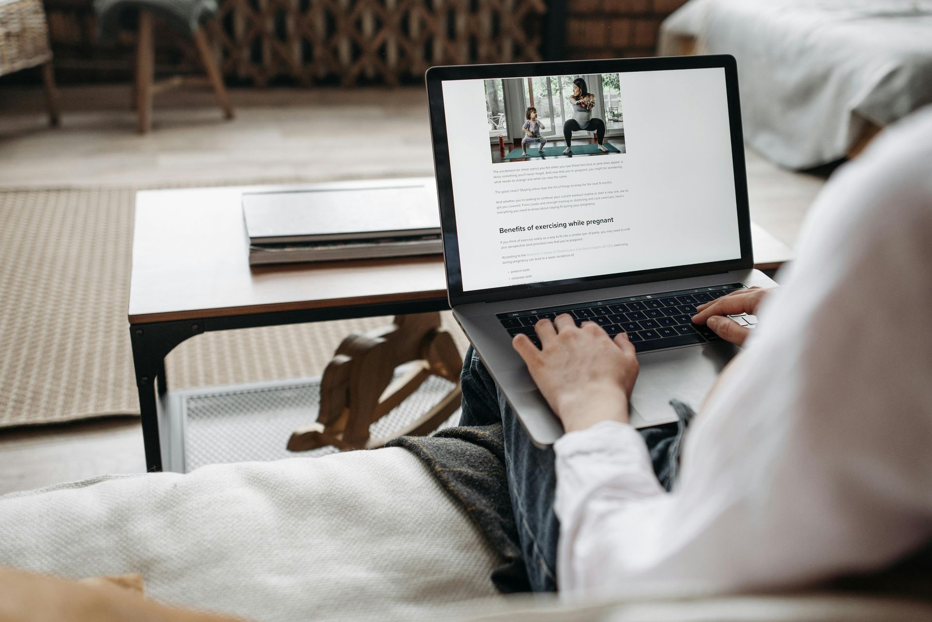 Person typing on laptop, viewing webpage with a yoga class video. In a home setting.