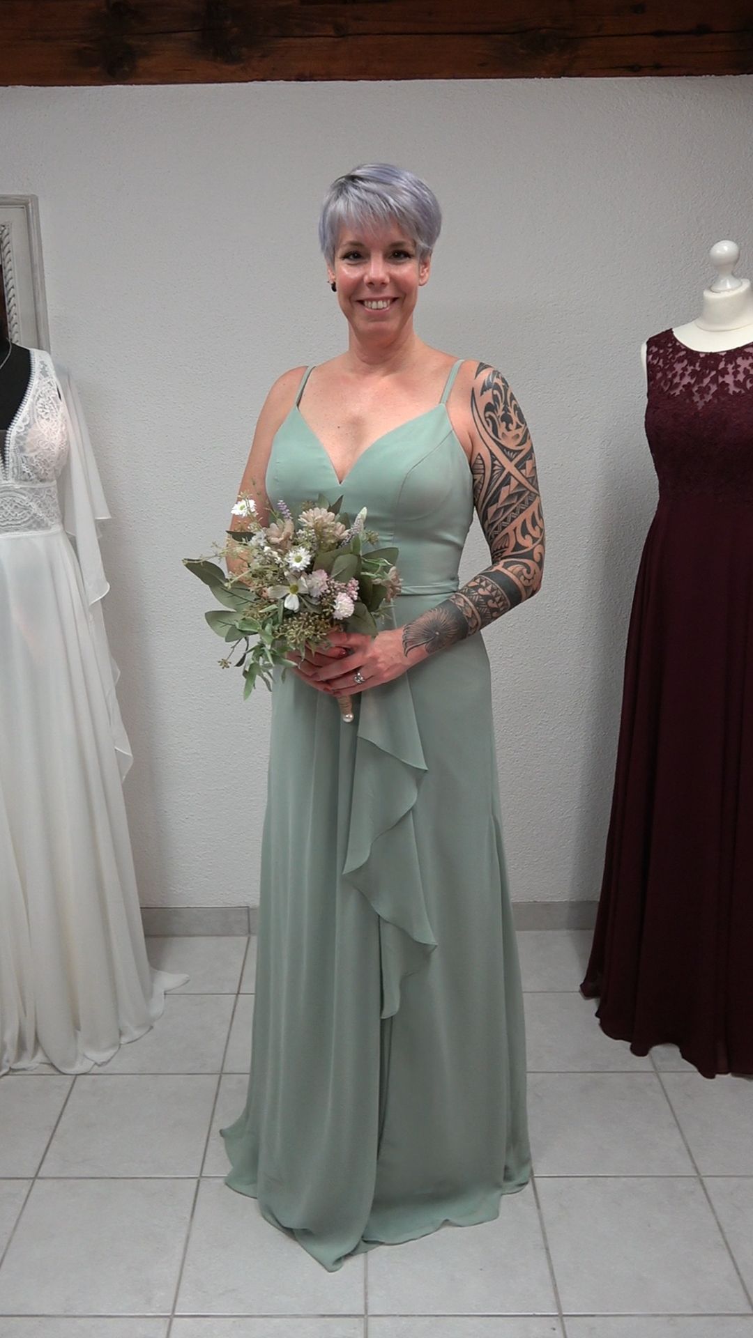 Eine Frau in einem grünen Brautjungfernkleid hält einen Blumenstrauß in der Hand.