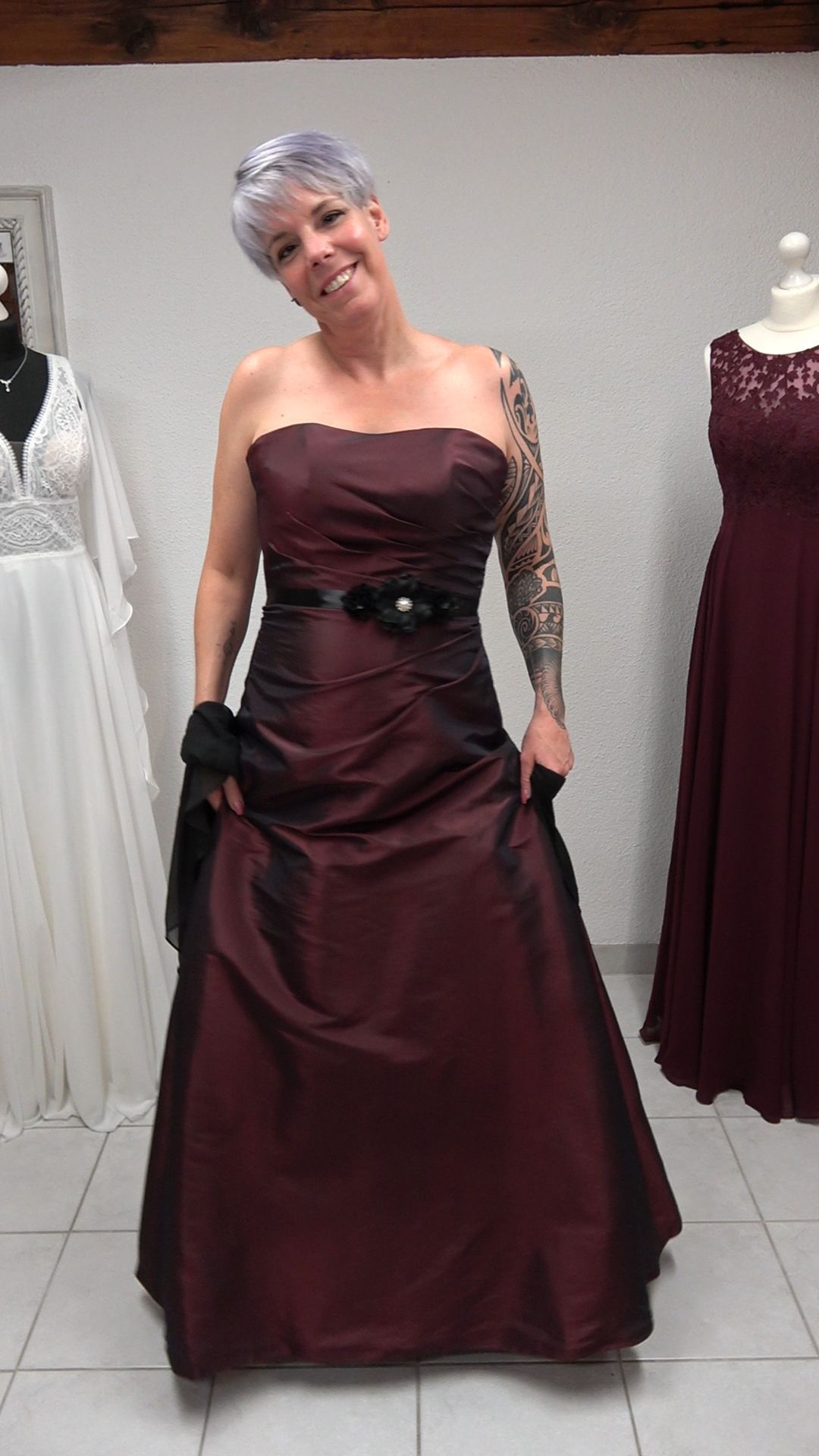 Eine Frau steht in einem Raum und trägt ein burgunderrotes und schwarzes Kleid.