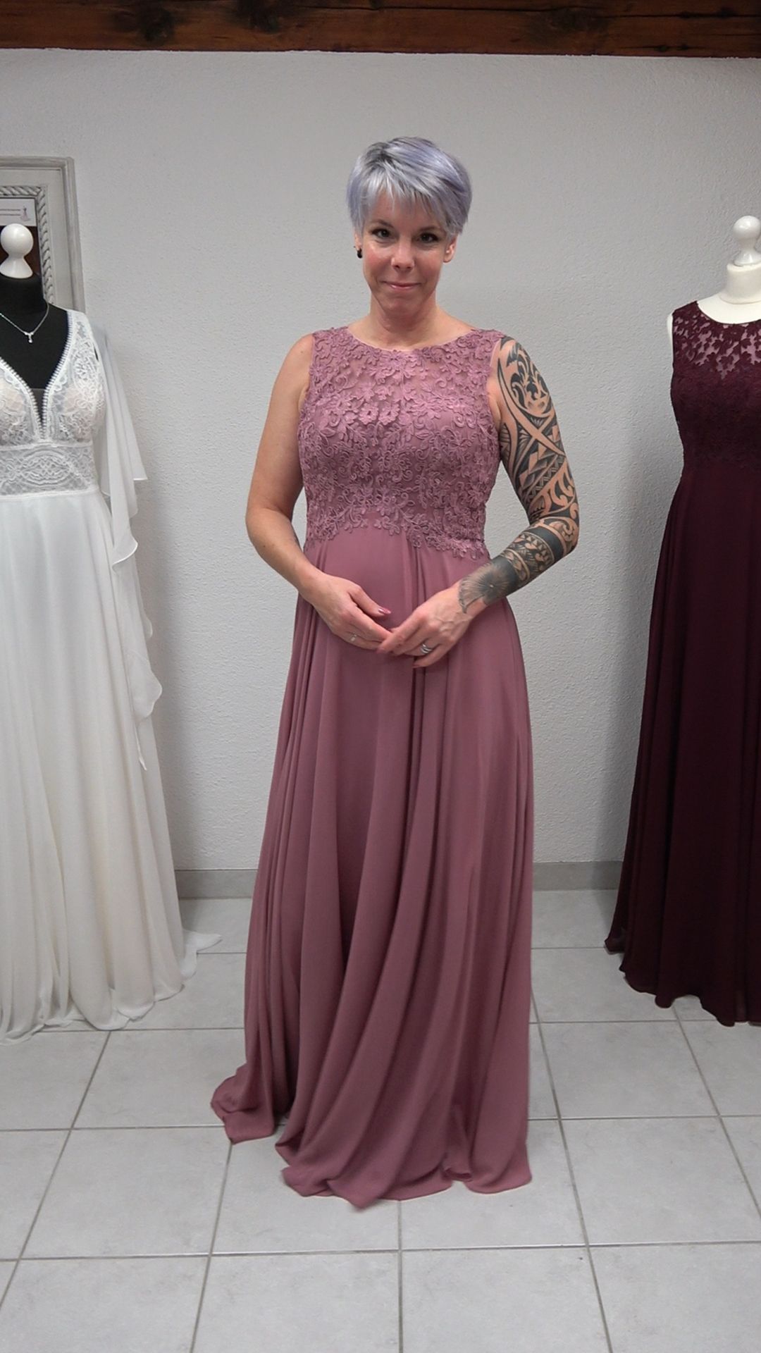 Eine Frau mit einer Tätowierung auf dem Arm trägt ein langes rosa Kleid.