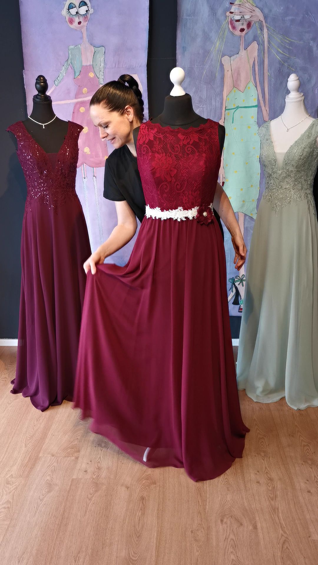 Eine Frau in einem burgunderfarbenen Kleid steht neben einer Schaufensterpuppe.