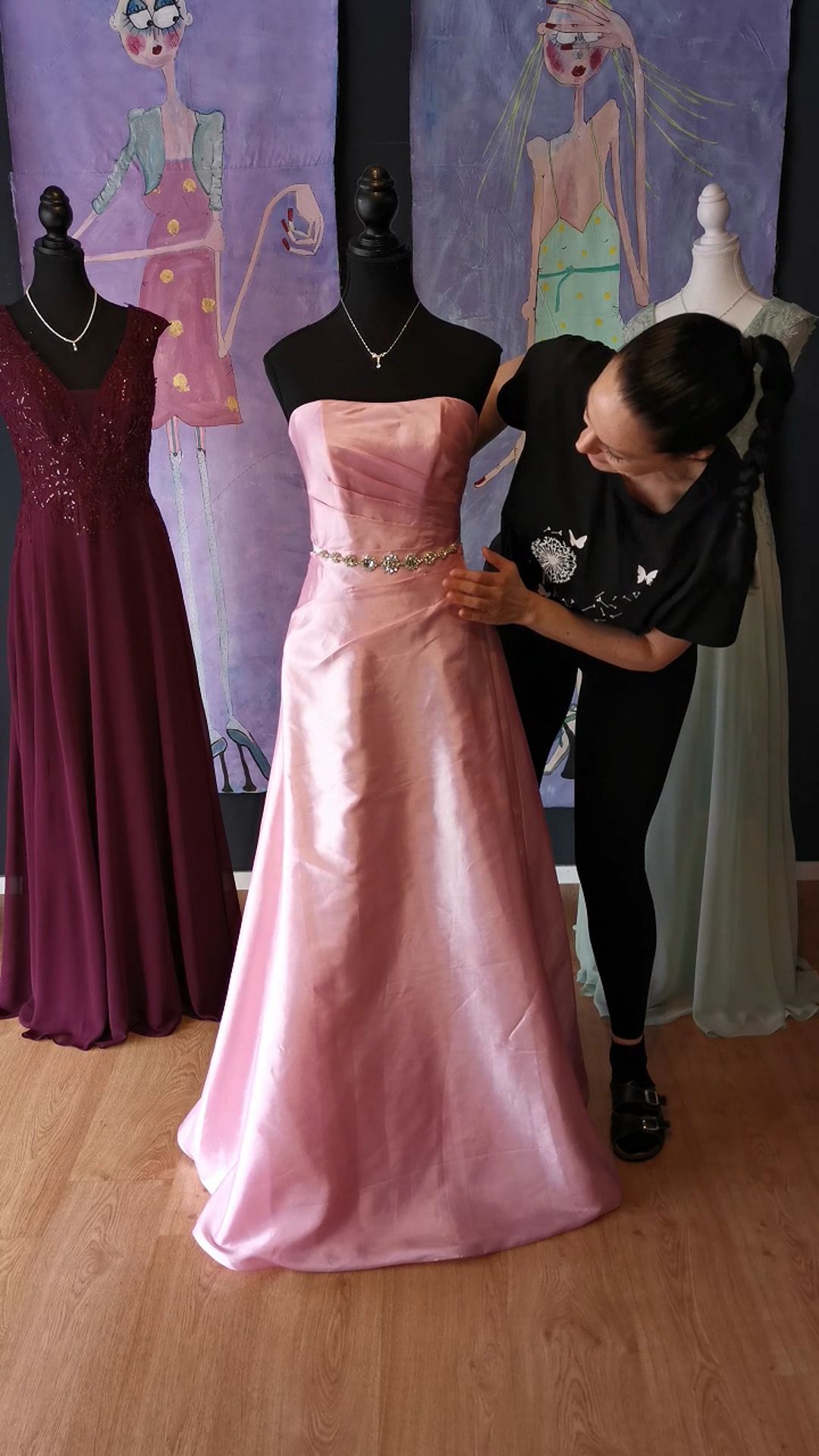 Eine Frau richtet ein rosa Kleid an einer Schaufensterpuppe.