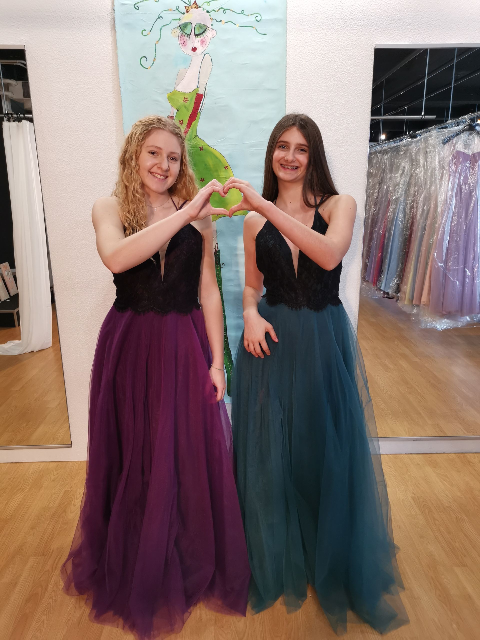 Zwei Frauen in langen Kleidern formen mit ihren Händen ein Herz.