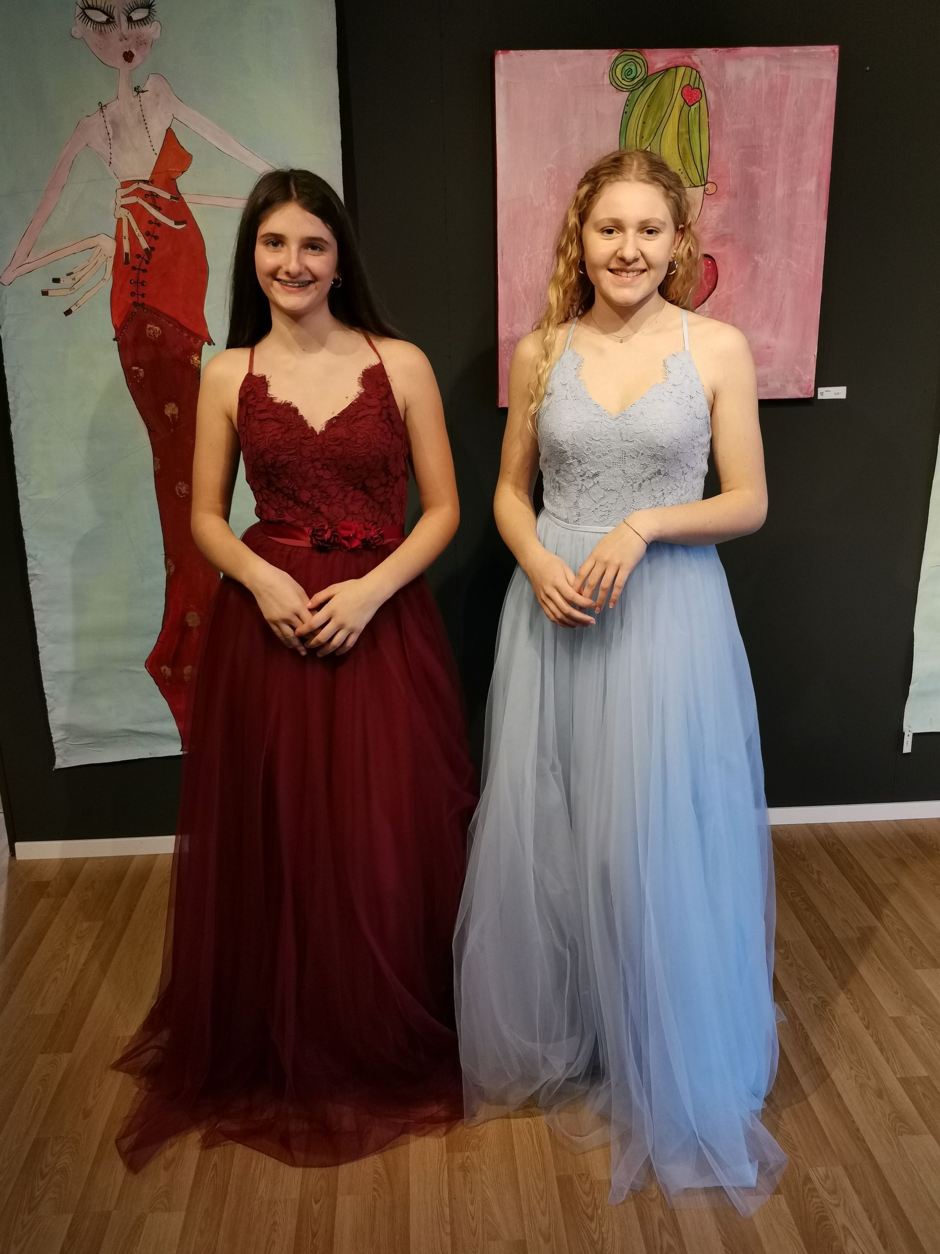 Zwei Frauen in langen Kleidern stehen nebeneinander vor einem Gemälde.