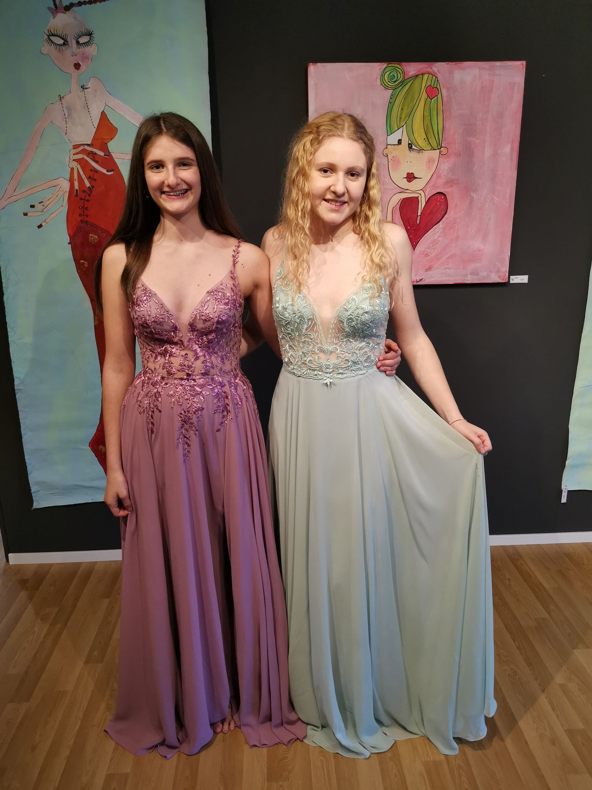 Zwei Frauen in langen Kleidern posieren vor Gemälden für ein Foto.