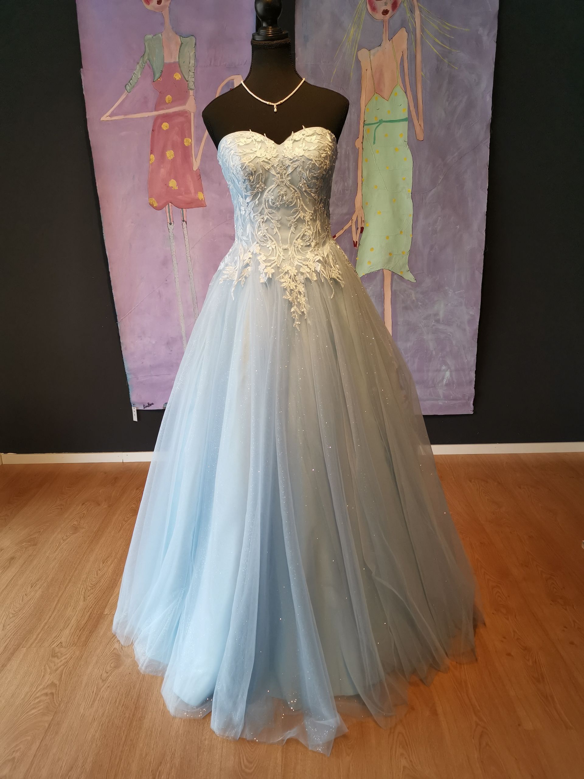 Eine Schaufensterpuppe trägt vor einem Gemälde ein hellblaues Ballkleid.