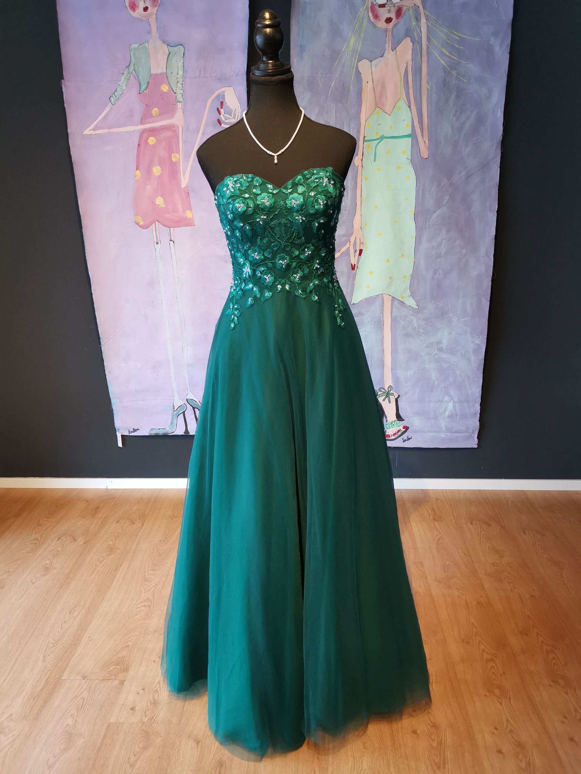 Vor zwei Gemälden hängt eine Schaufensterpuppe in einem grünen Kleid.