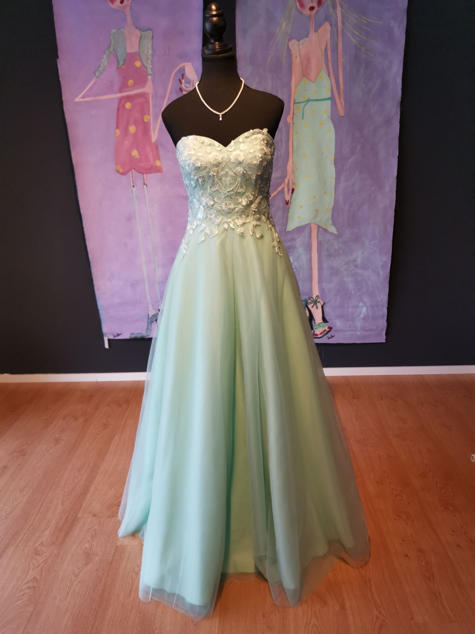 Eine Schaufensterpuppe trägt ein mintgrünes Kleid vor einem Gemälde.