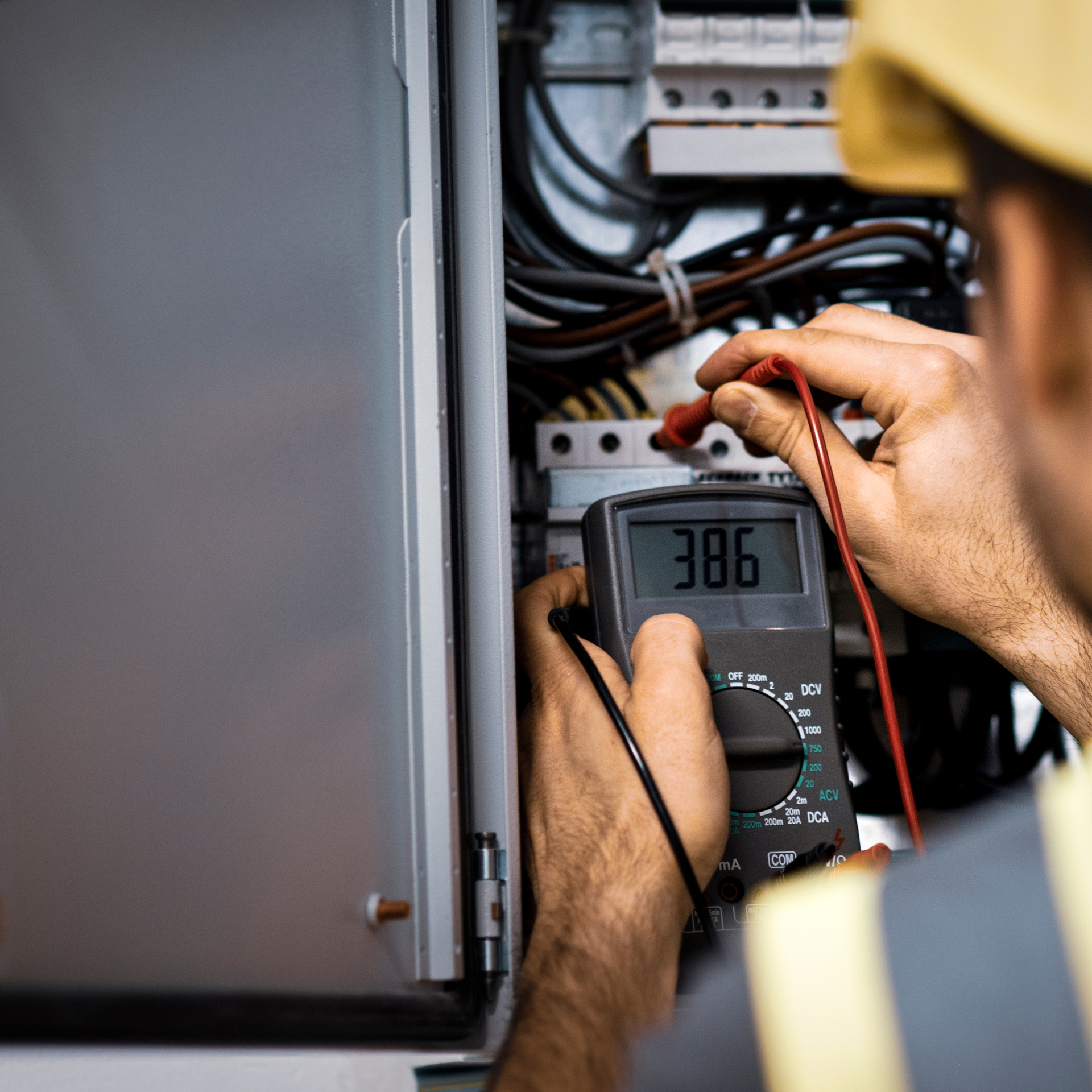 Electrician using a multimeter to measure voltage in an electrical panel, display reads 386.