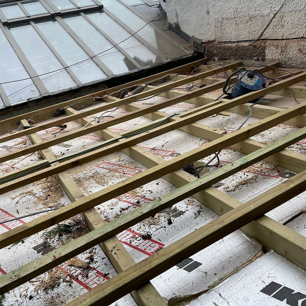 Wooden roof structure under construction, with insulation between beams. A power saw sits on top.
