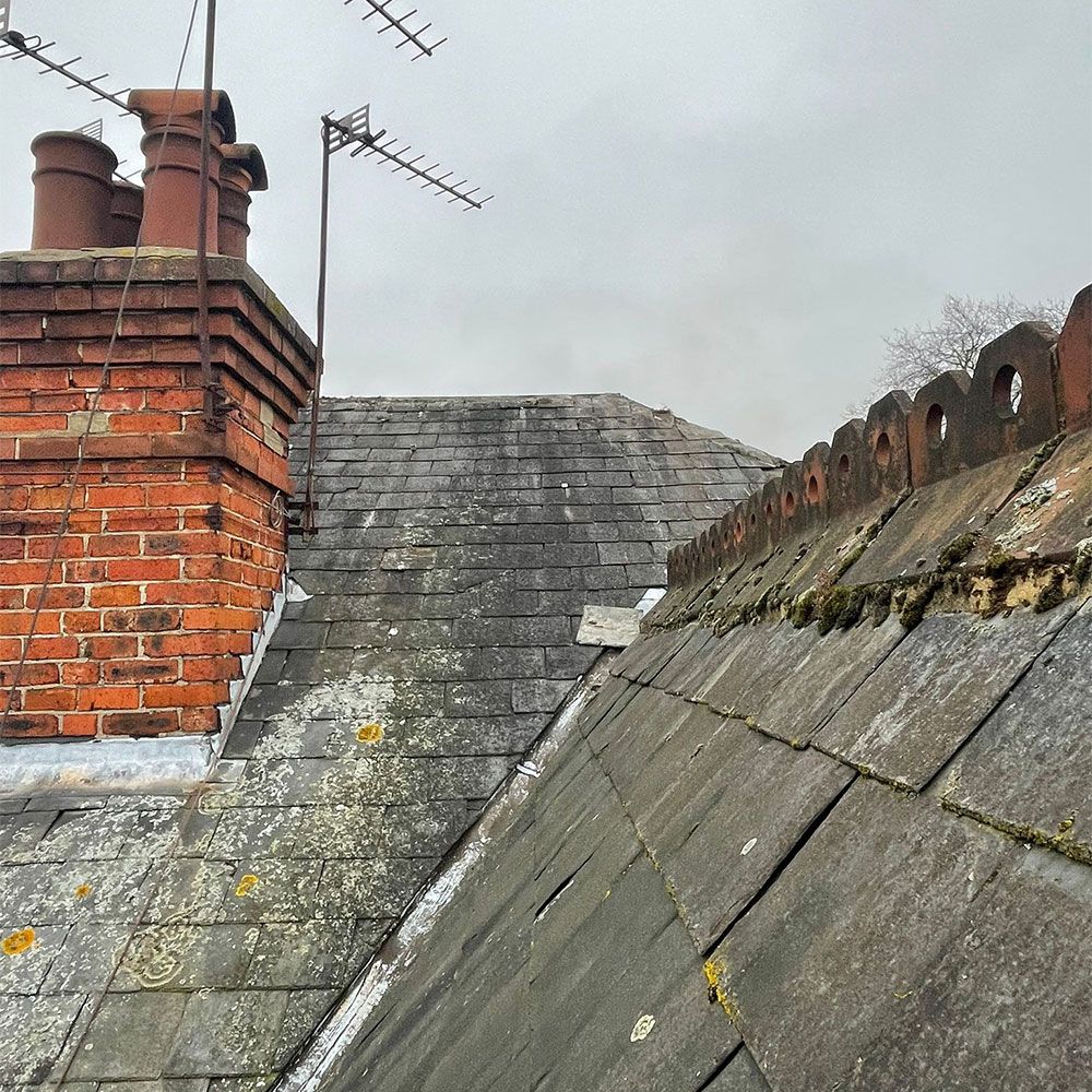 Brick chimney and slate roofs with an antenna under a cloudy sky.