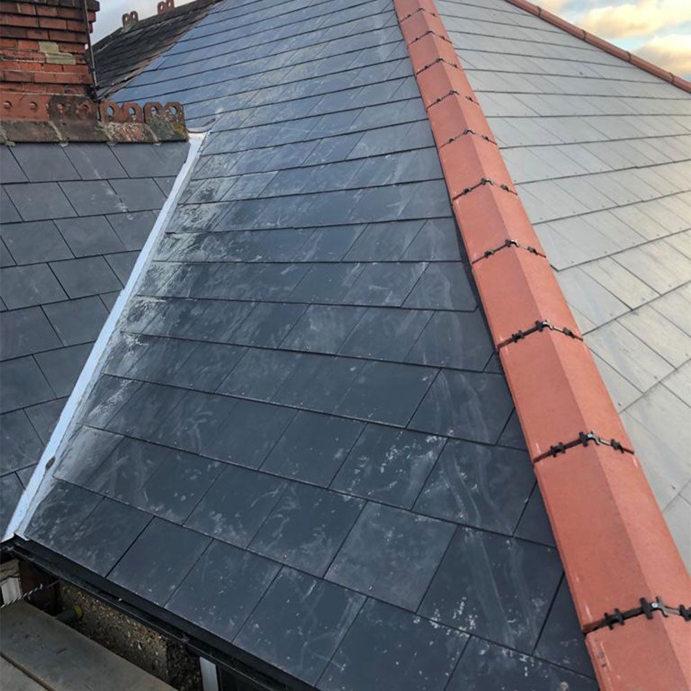 View of a roof with dark gray slate tiles, red ridge tiles, and a white gutter.