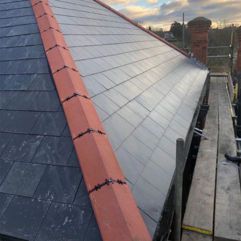 Completed slate roof with red ridge tiles and scaffolding.