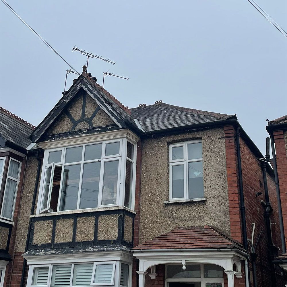 Two-story brick house with a bay window, chimney, and antenna on a cloudy day.