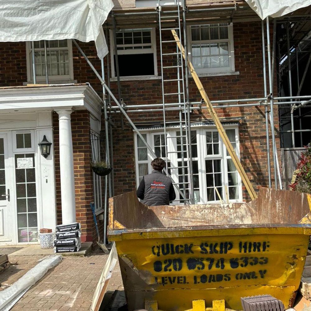 A person near a yellow skip bin in front of a brick house with scaffolding.