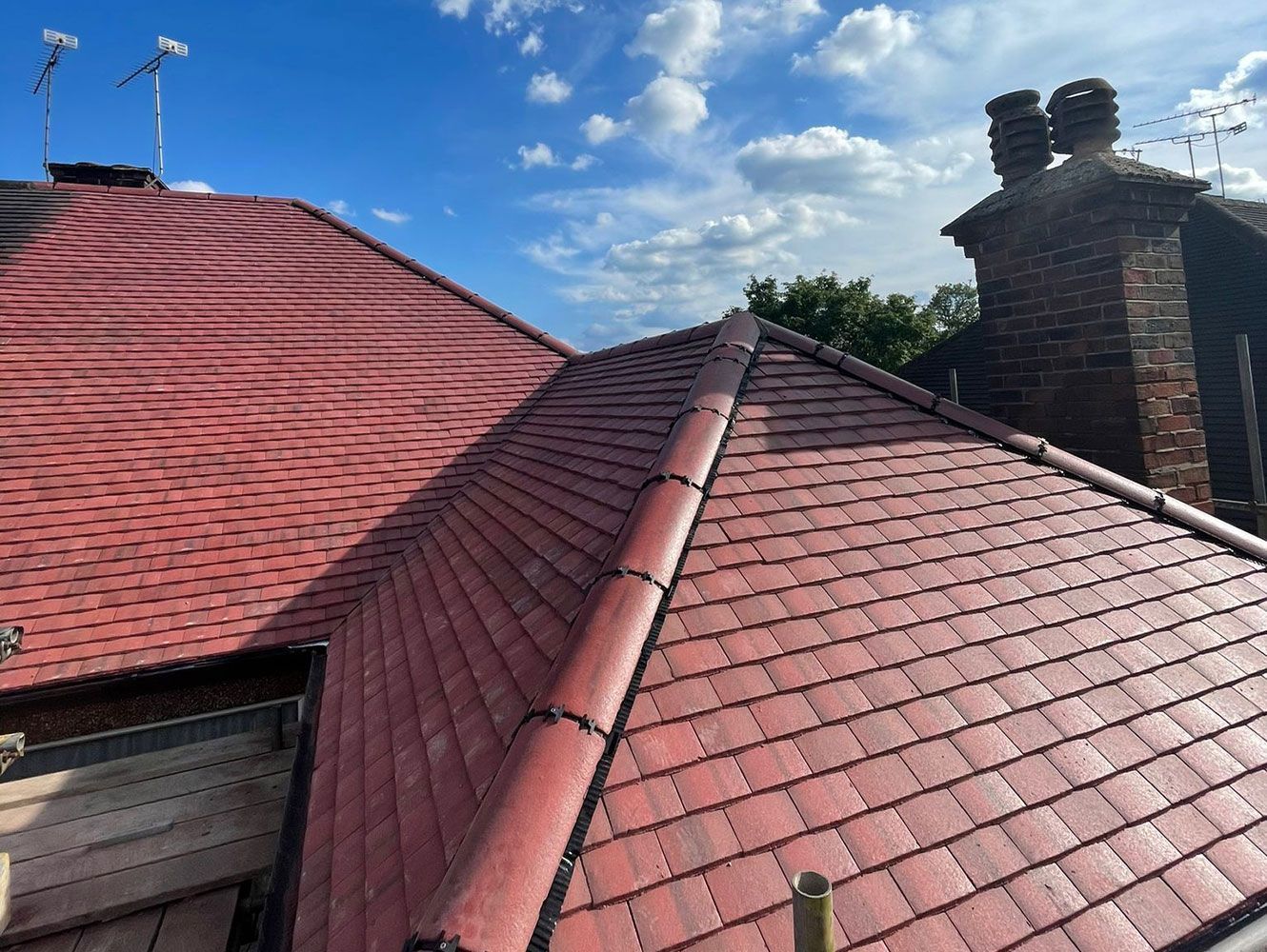 Red tiled roof on a sunny day with a chimney and blue sky in the background.