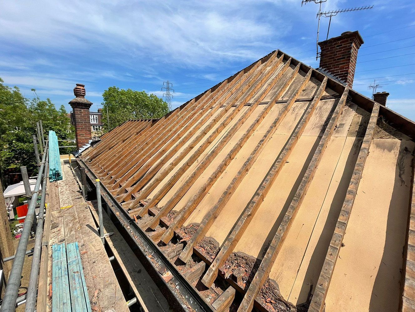 Rooftop under construction, exposing wooden beams, brick and scaffolding under a blue sky.