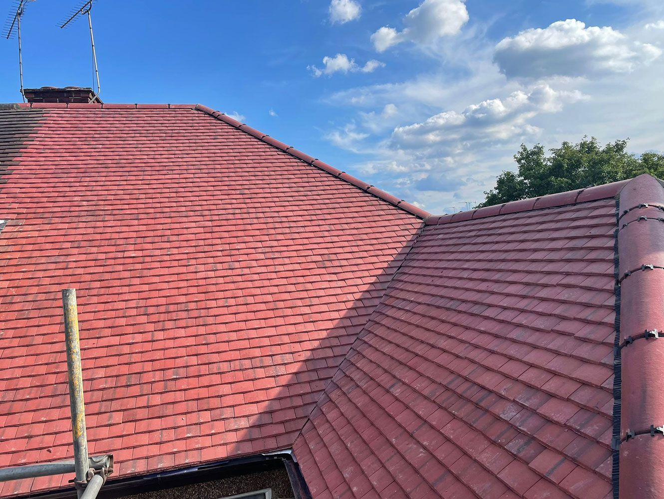 Red tiled roof against a blue sky with clouds; scaffolding visible.
