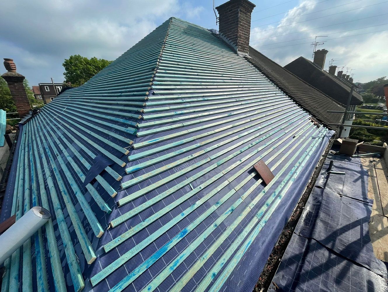 A blue and green metal roof with horizontal lines, partially covered by a tarp.