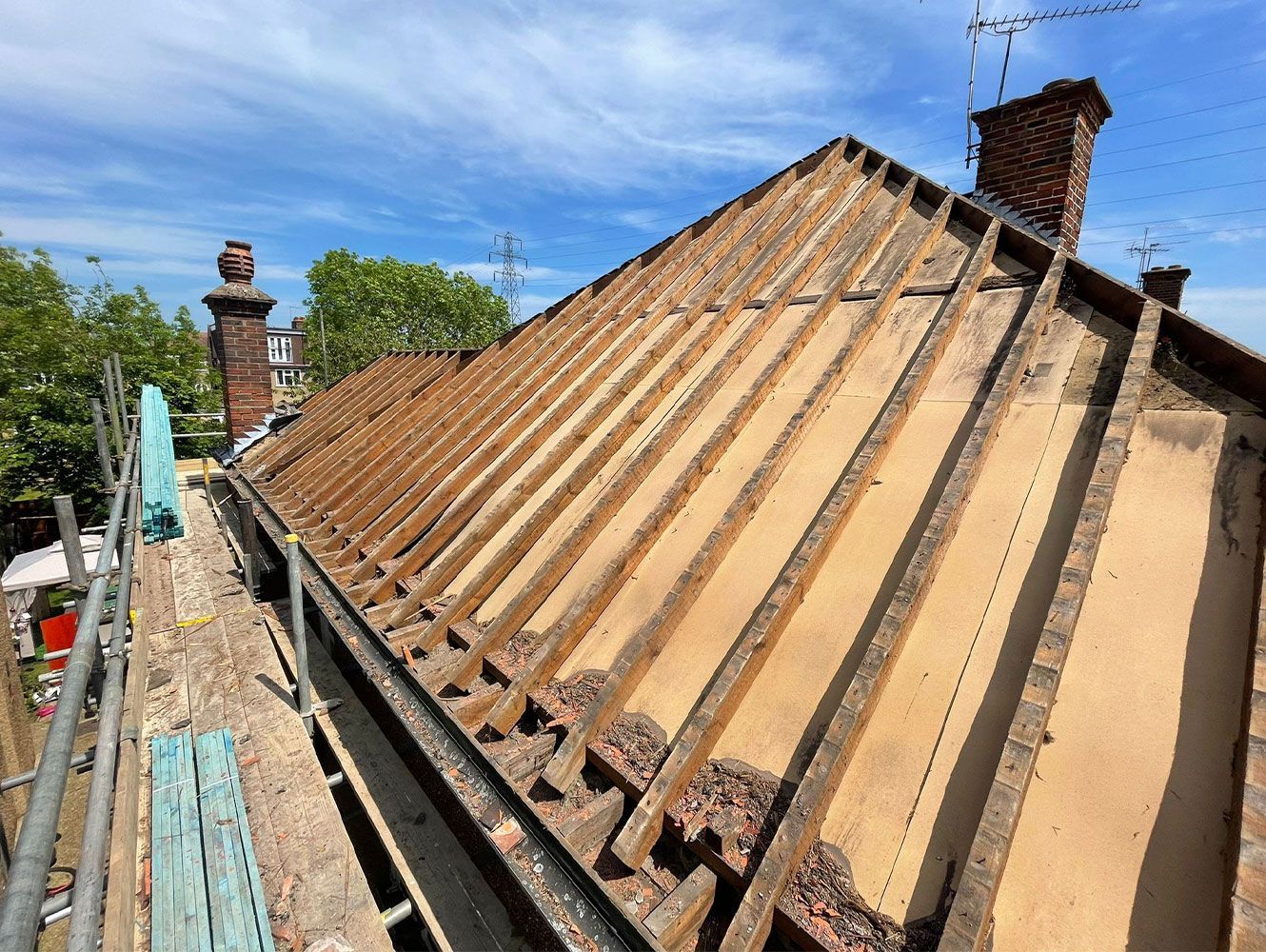 Roof with exposed rafters and scaffolding under a blue sky.