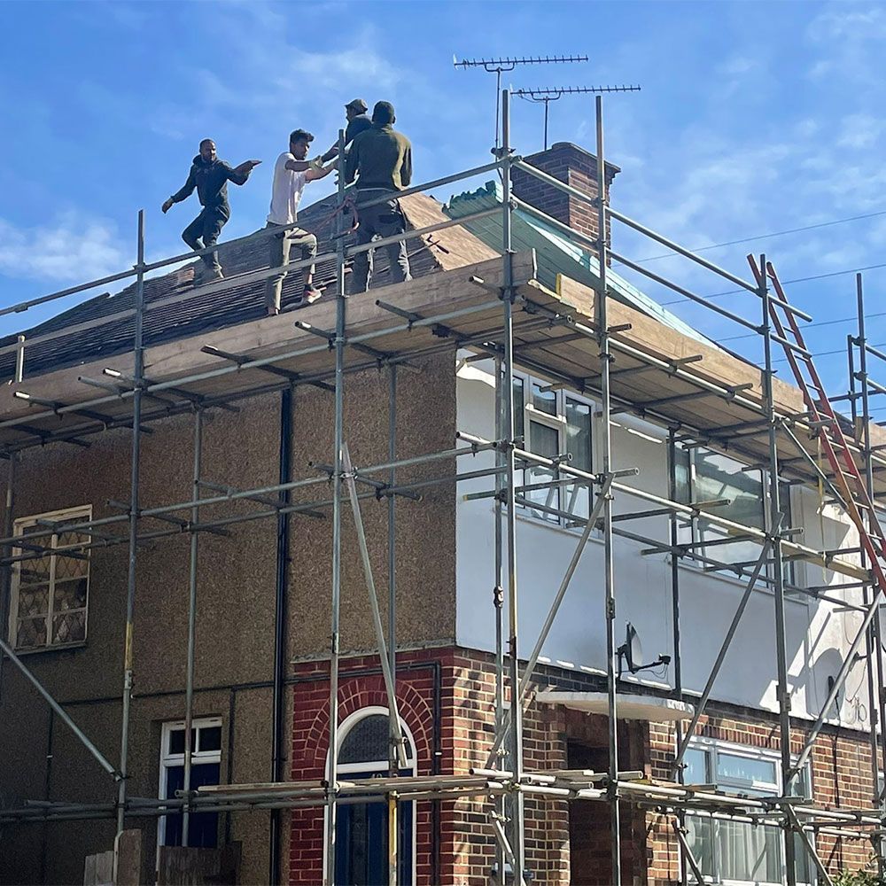 Workers on roof with scaffolding. House exterior under renovation, clear sky.