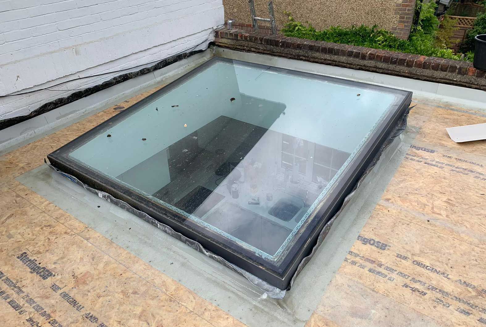 Skylight on a flat roof, rectangular glass with a dark frame, surrounded by roofing material.