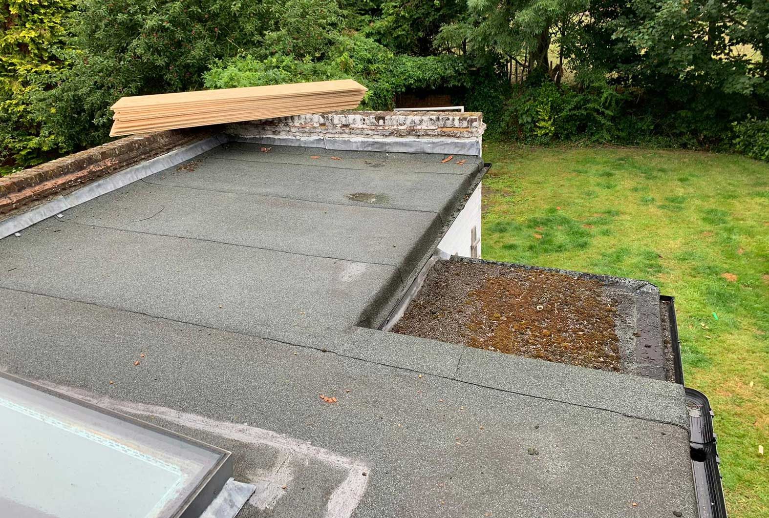 Flat roof with weathered surface, wooden beam, and grassy background.