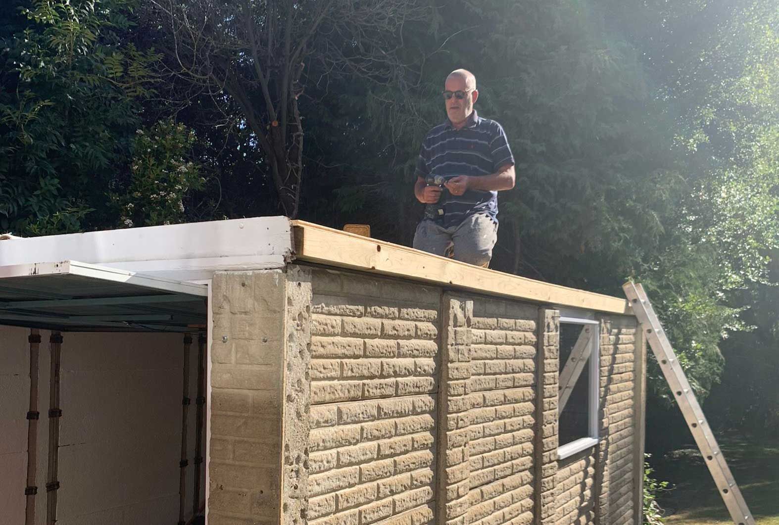 Man on a shed roof, adding boards. Building outdoors, sunny.