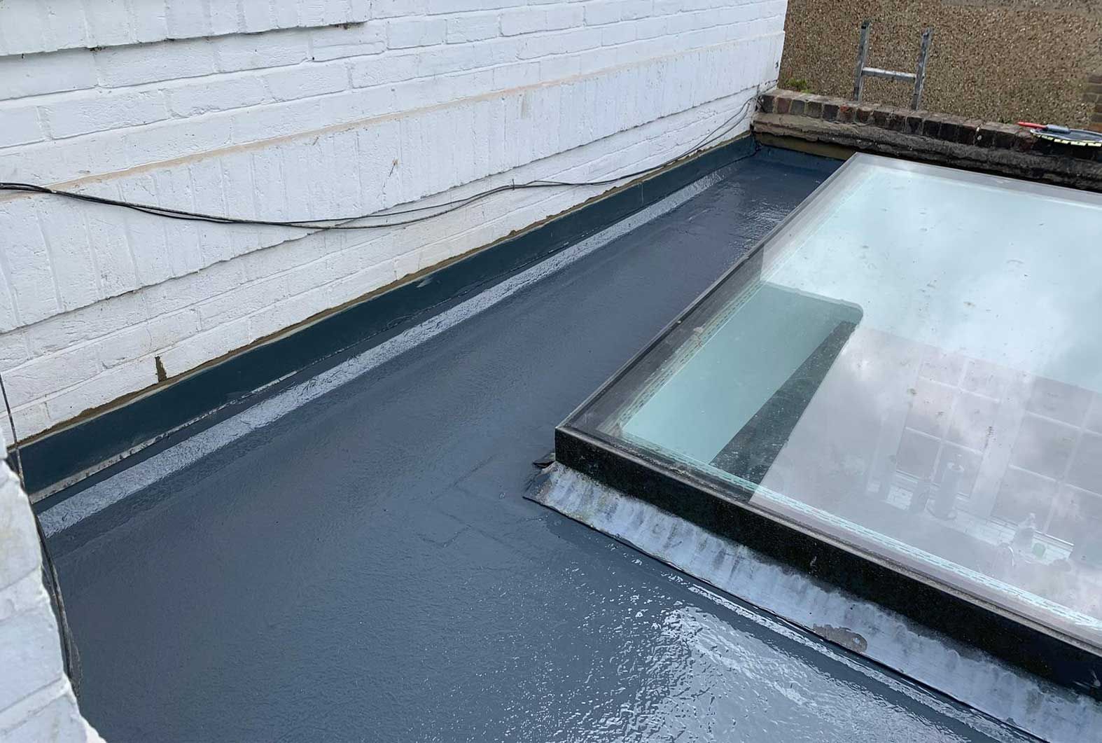 Dark gray, flat roof with a skylight and white siding.