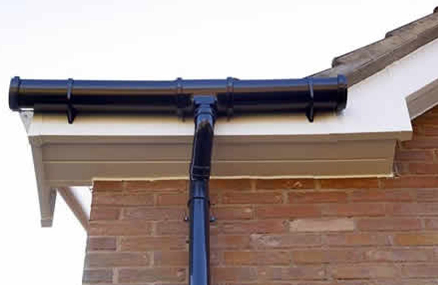 Black gutter system attached to a white soffit on a brick building.