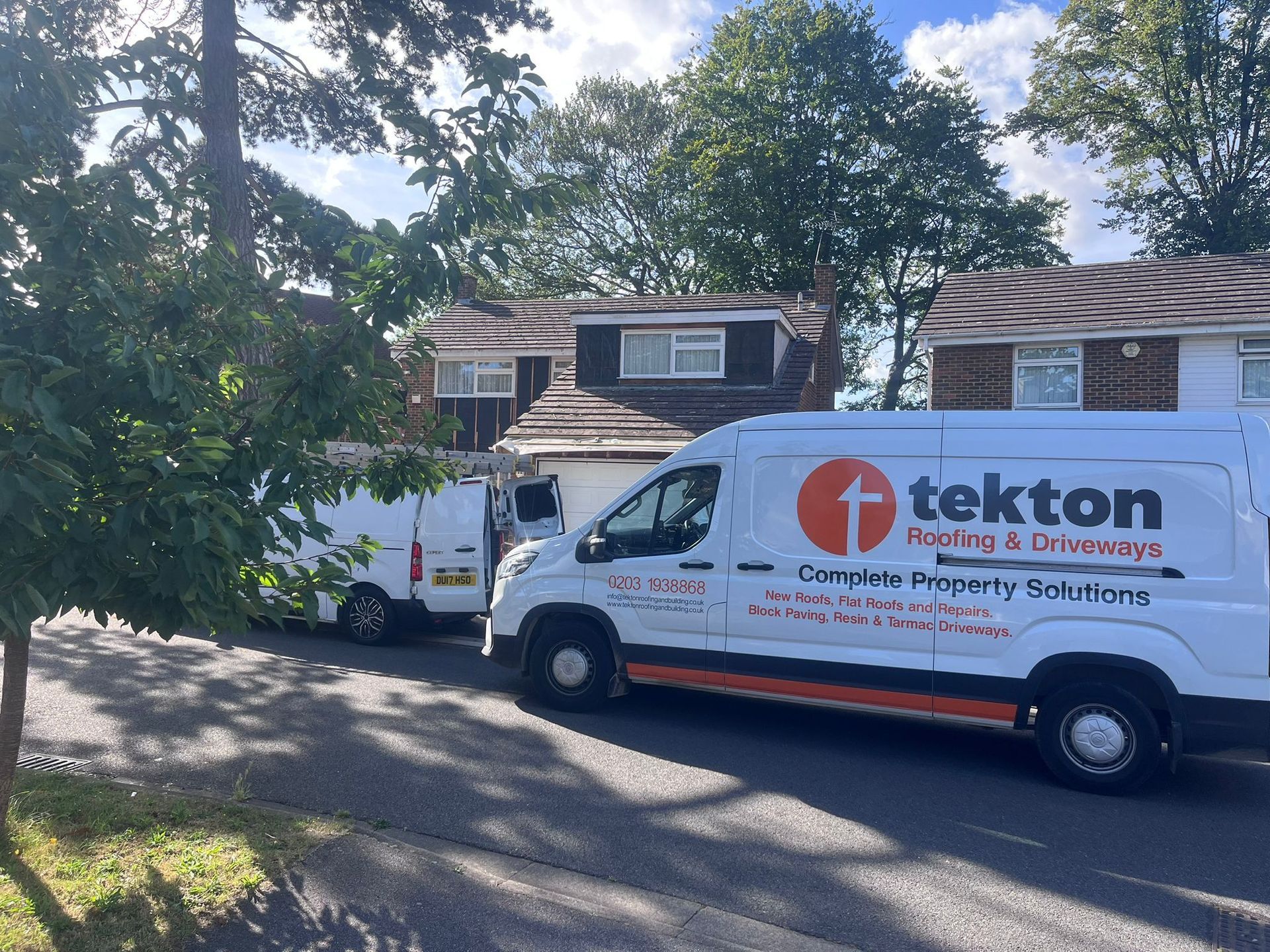 Two white Tekton vans parked on a residential street in front of a house.